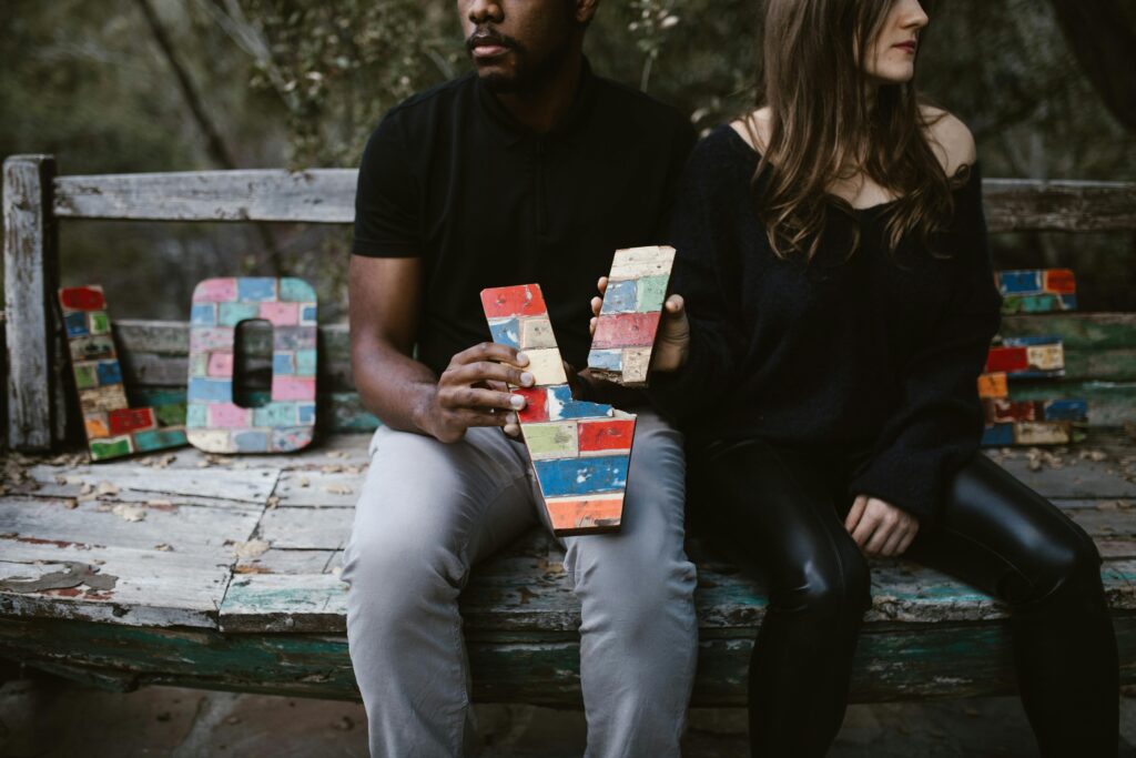 A couple holding colorful wooden letters on a rustic bench outdoors.